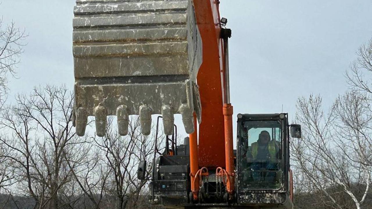 A large digging machine on top of a pile of rocks outside.