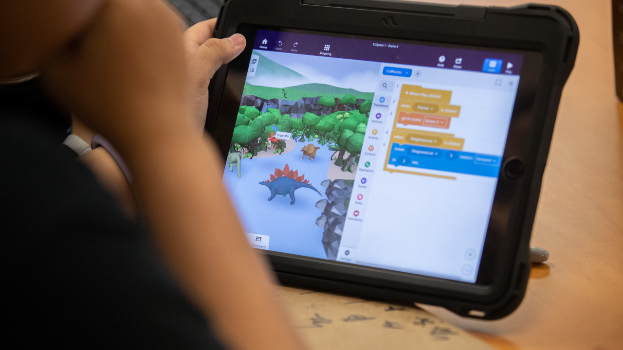 A young child looking at a tablet open to a screen with dinosaurs and text