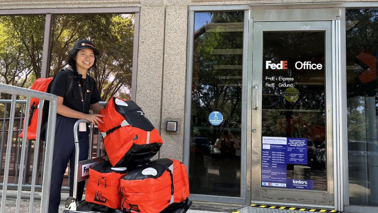 Someone rolling red bags on a trolley to a FedEx office