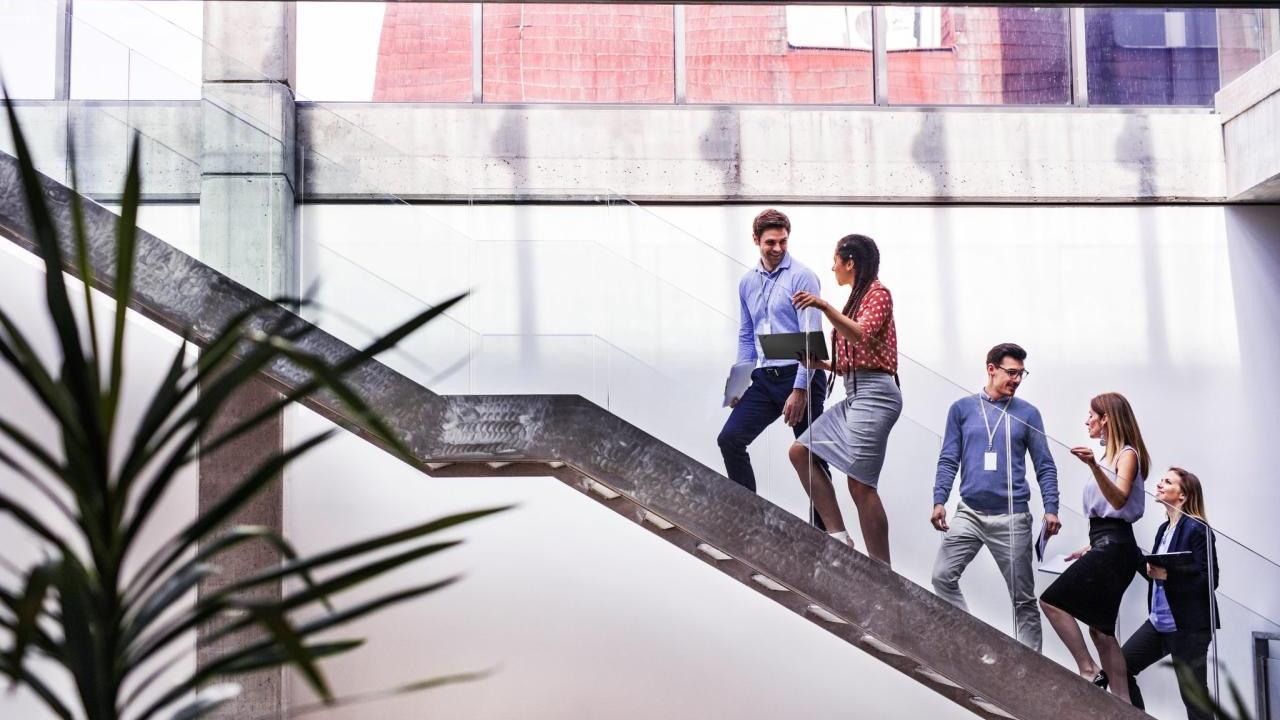 People talking while climbing a staircase with clear railing sides.