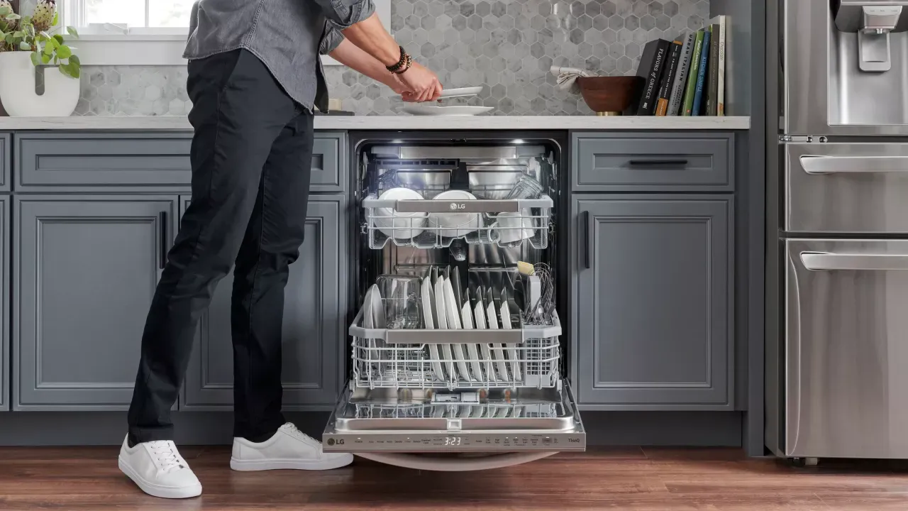 A person unloading clean dishes from a LG brand dishwasher in a kitchen.
