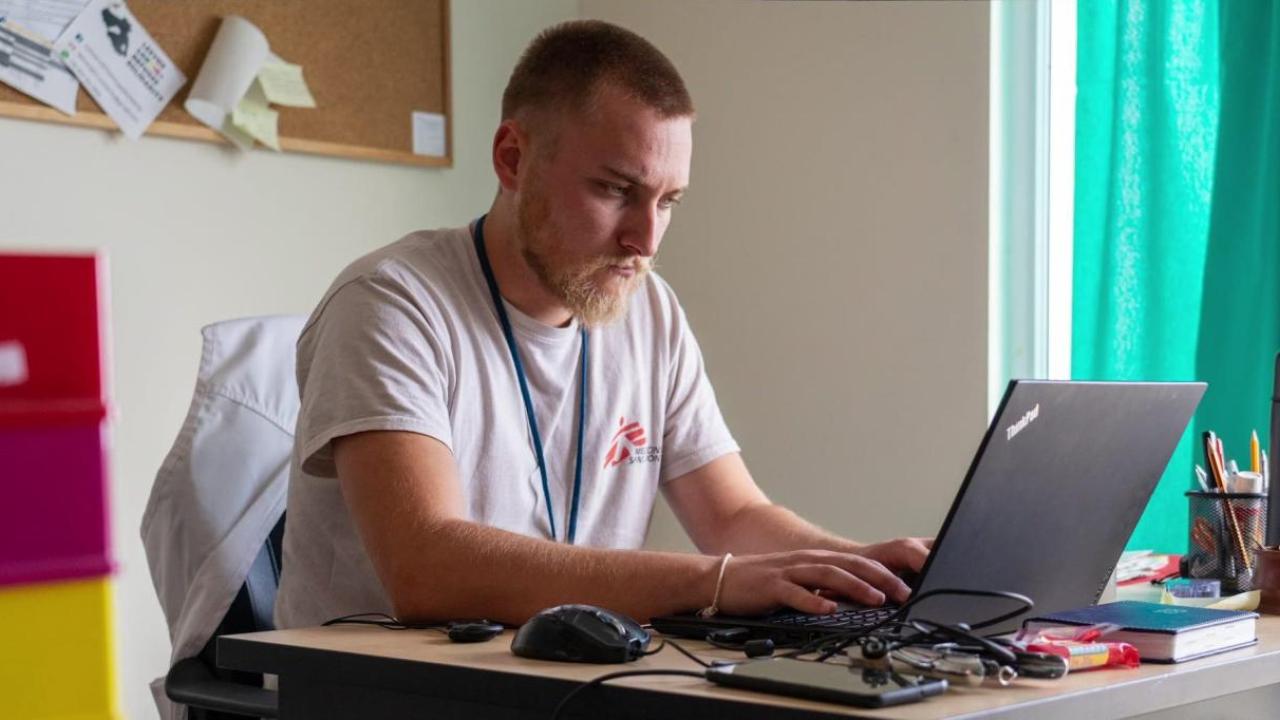 A person seated, working on a laptop in an office setting.