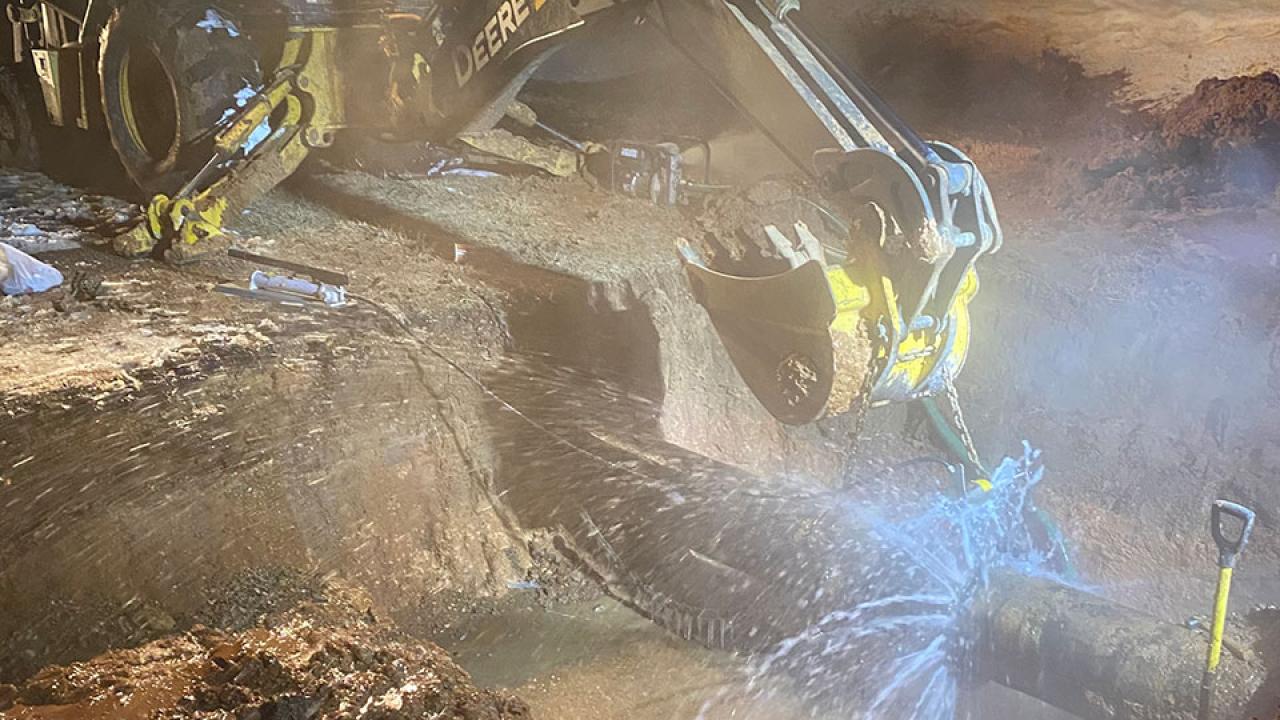 a backhoe poised over a burst water pipe
