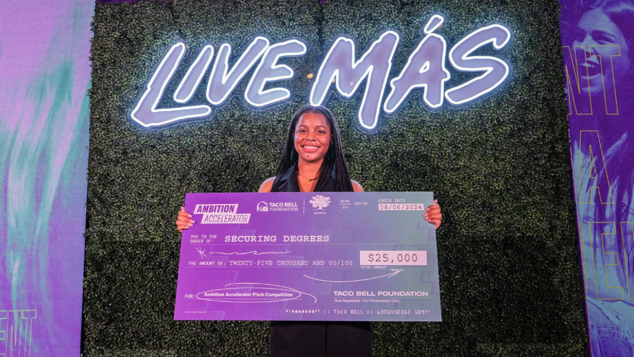 A person holding an oversized check in front of a wall that says "Live Mas"
