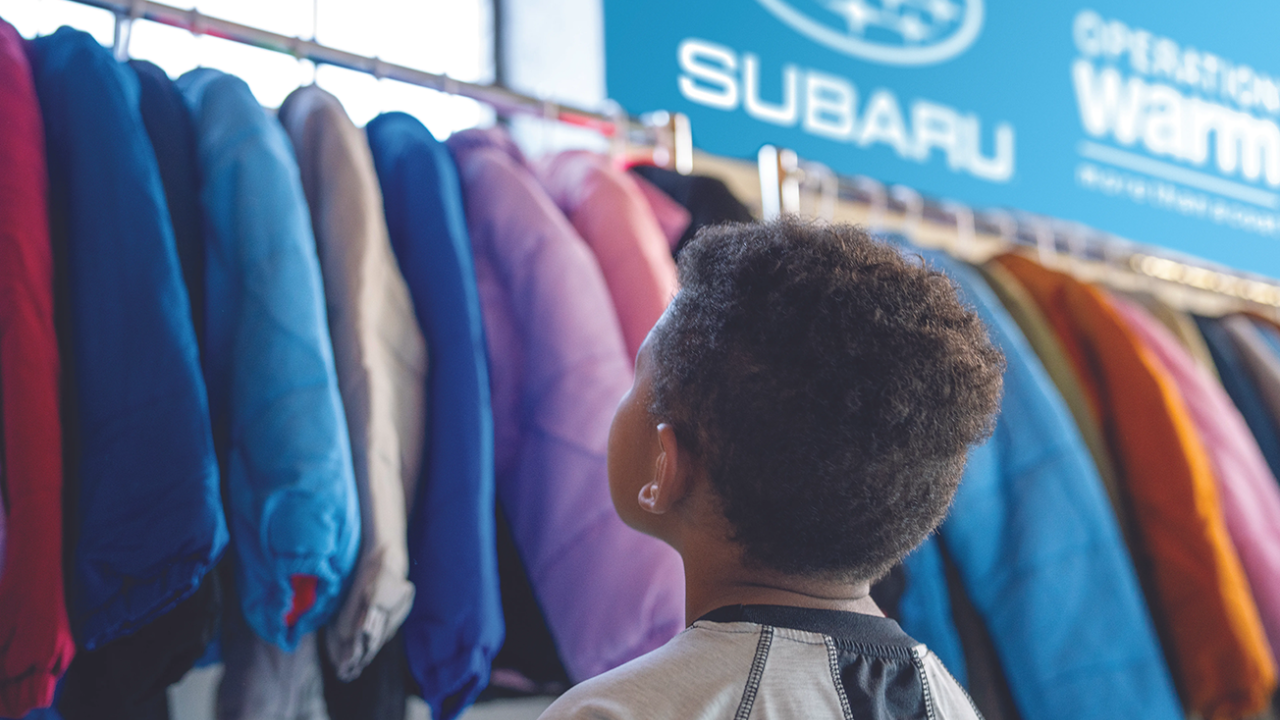 child looks up at hanging coats