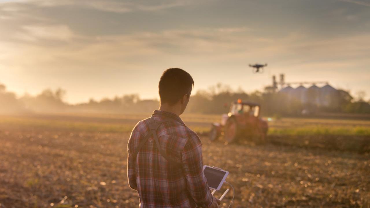 A farmer using a controller to fly a drone over farm fields.