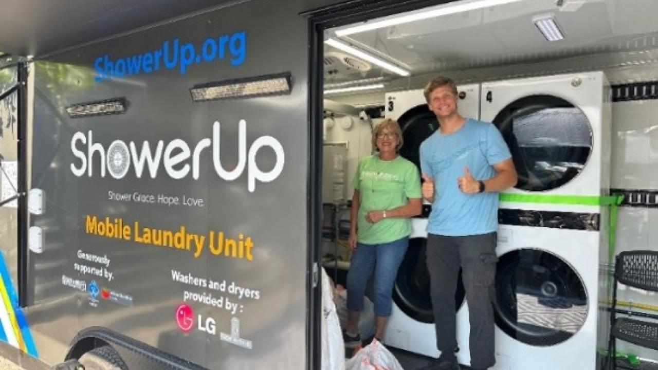 Two people smiling inside an open ShowerUp mobile laundry unit