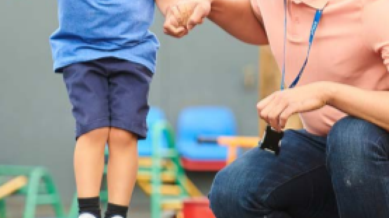 An adult holding a child's hand as they jump along colored spots.