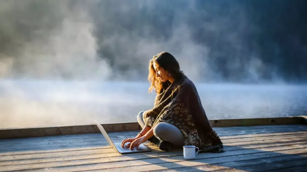 Woman sitting on a foggy dock with a laptop and cup of coffee