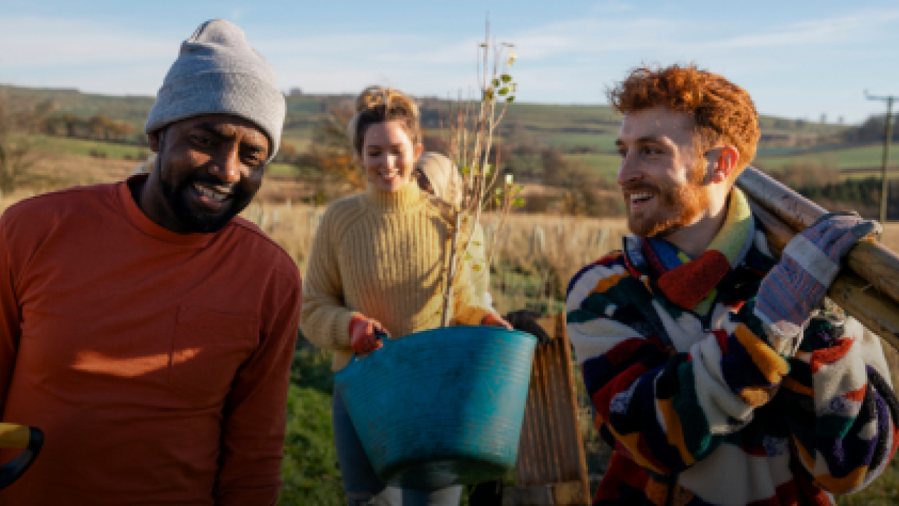 "earth month Powering Sustainable Journeys" Three people walking in a field, carrying gardening tools.