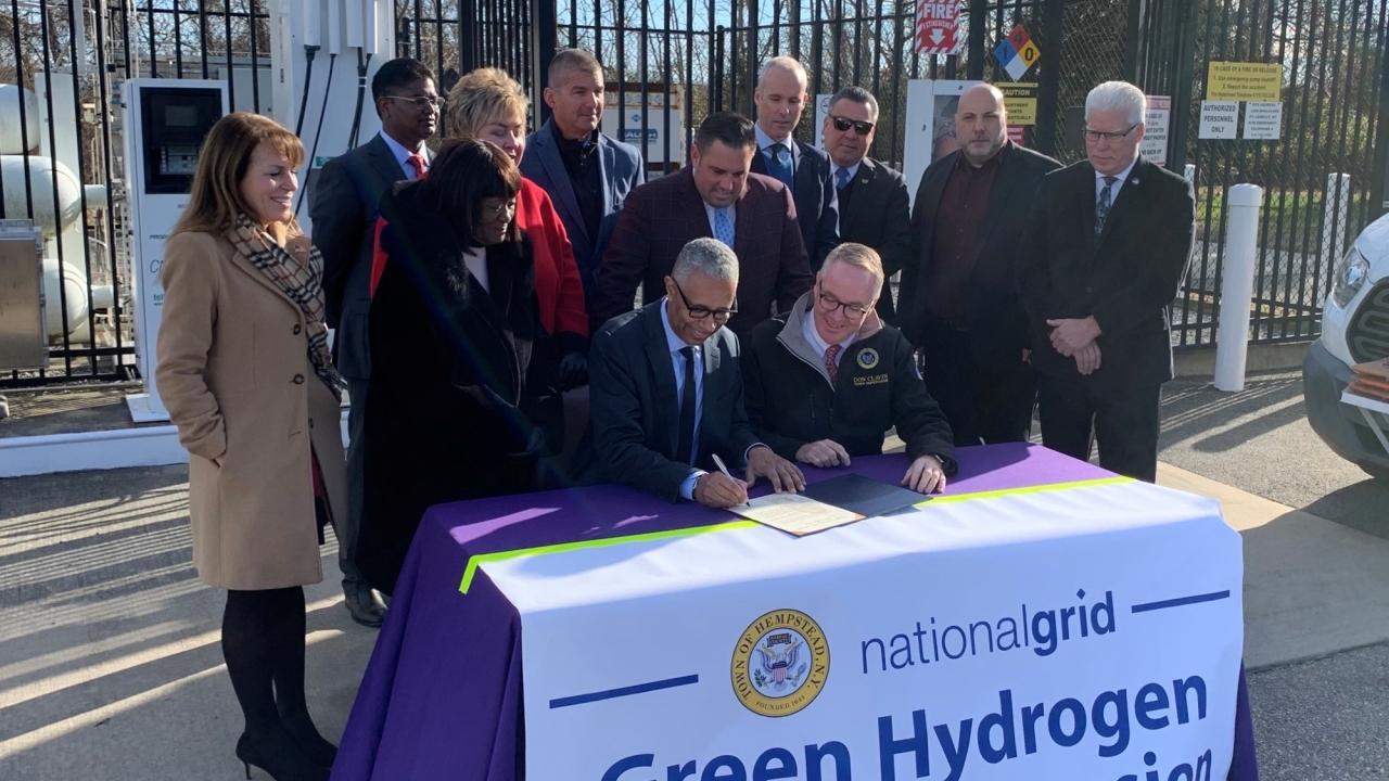 People posing for picture around table with banner reading: Green Hydrogen Facility Expansion