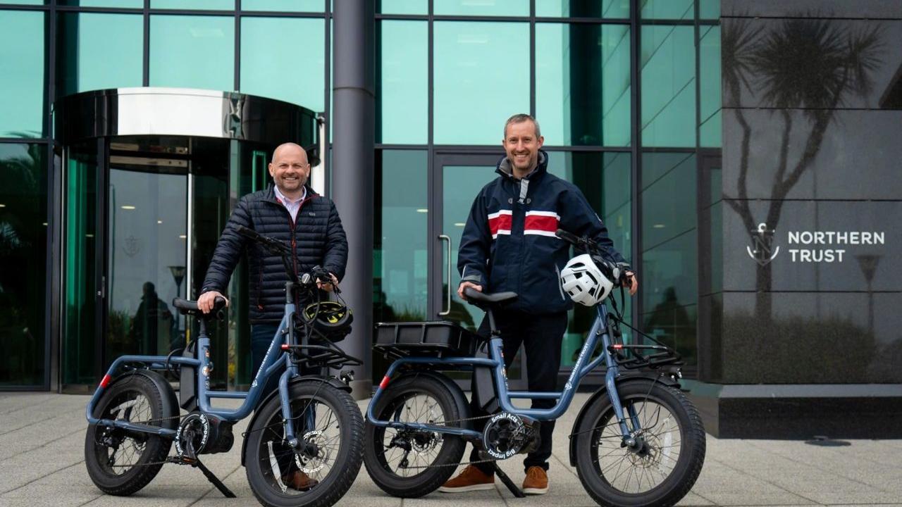 Pete Bowker and Daniel Usher posed by e-bikes outside a Northern Trust building.