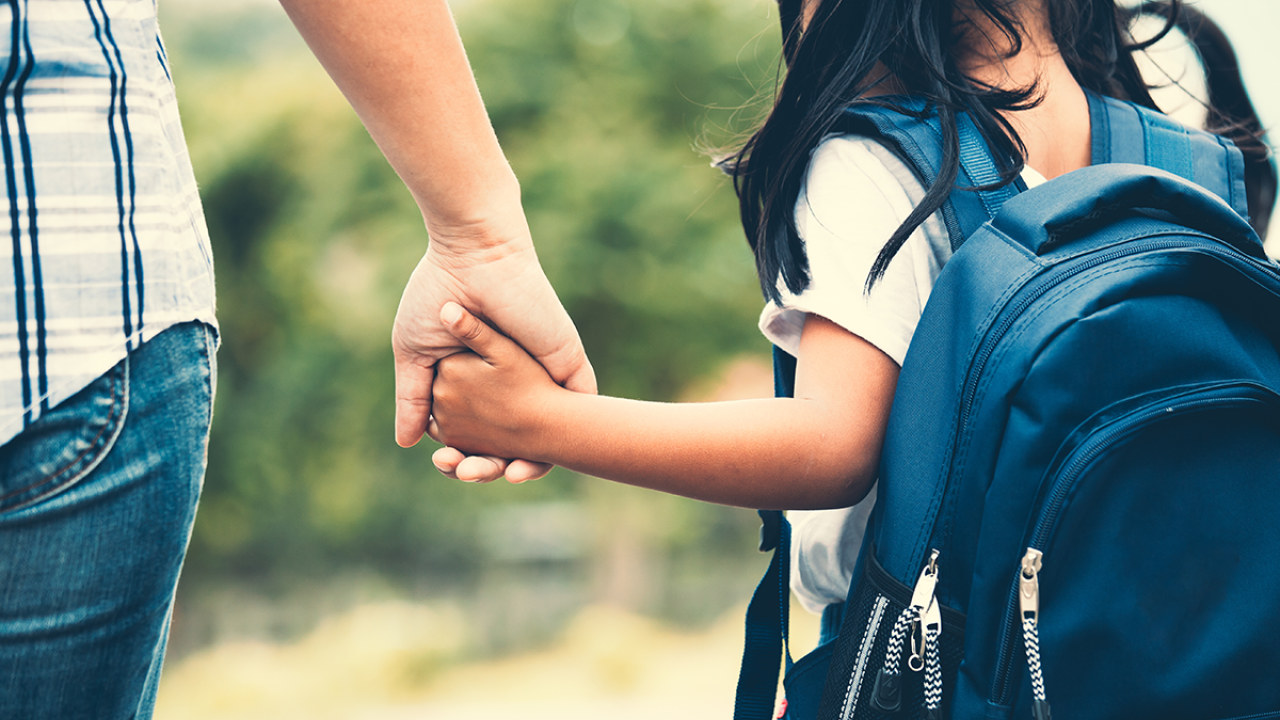 child wearing a backpack holding a grown-up's hand