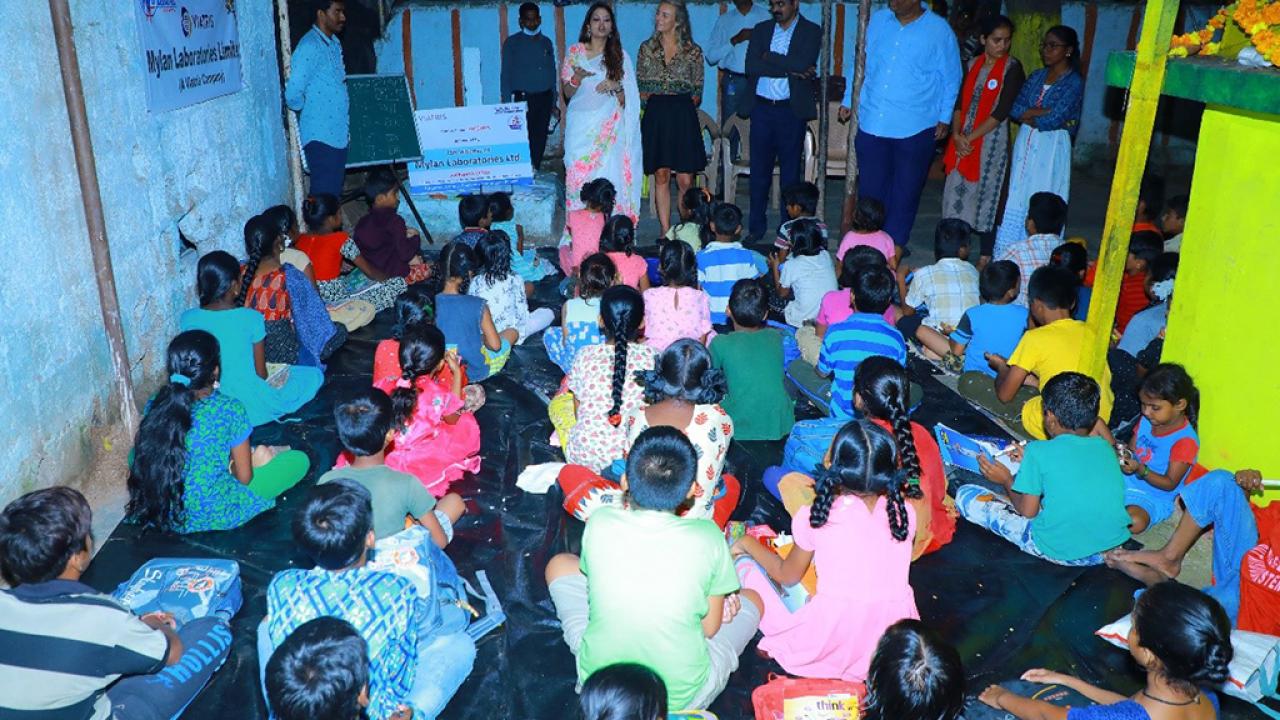 A group pf students, seated, adults standing at the front of the room.