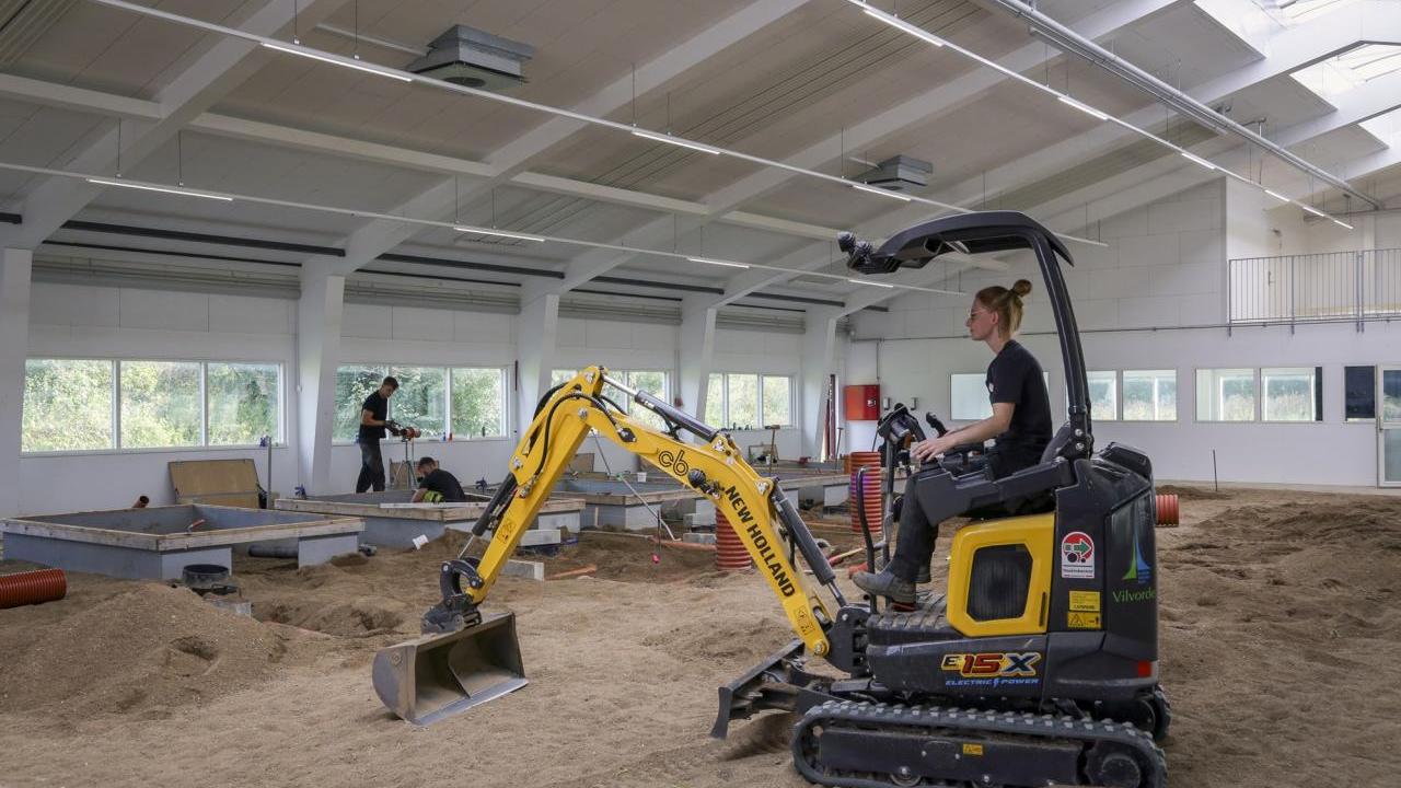 A person driving a digging machine in an enclosed sandy area.