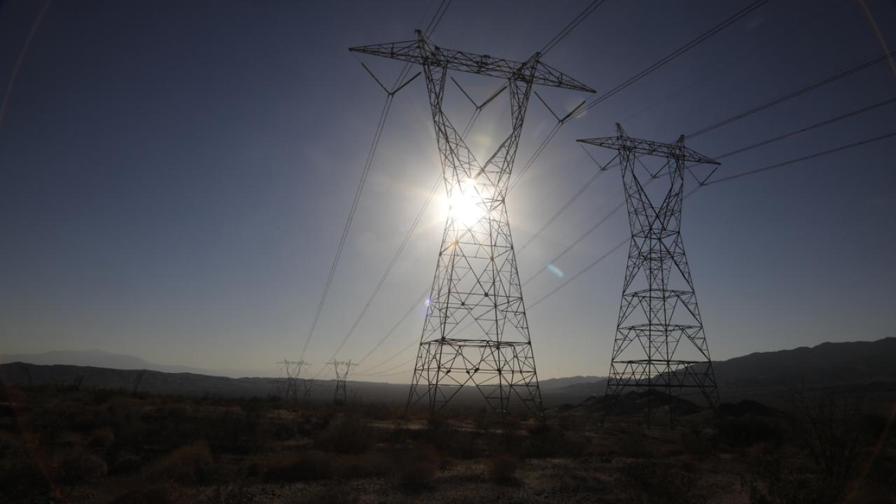 Tall power lines lined up with the sun over a large flat open landscape