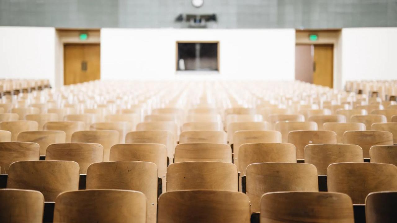 An empty auditorium with rows of wood back seats.