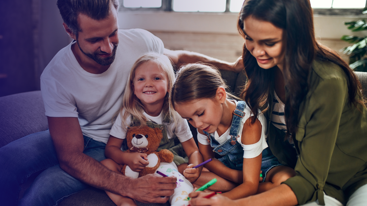 Two adults sitting on a couch with two children writing on stuffed bears