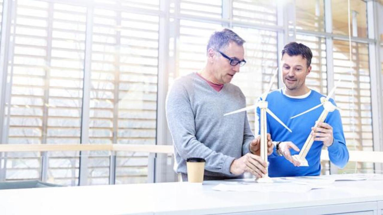 Two people holding small models of wind turbines in an open space.