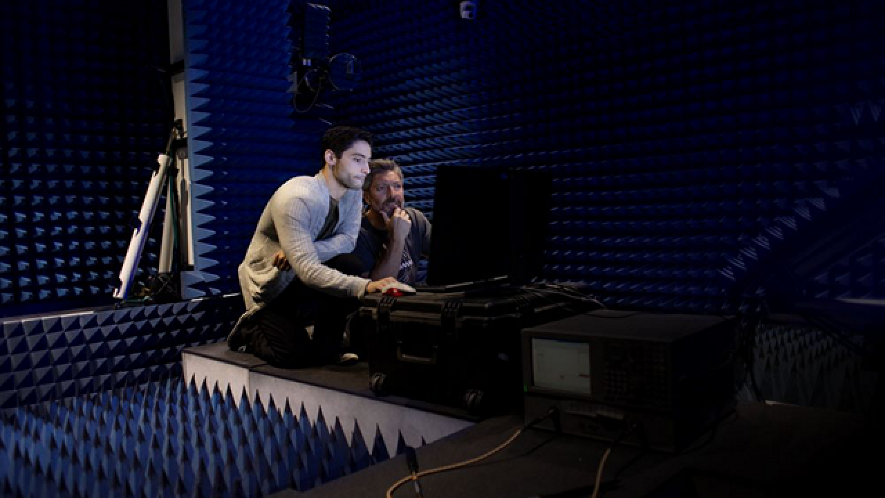 Two people surrounded by soundproof foam looking at the same computer screen.