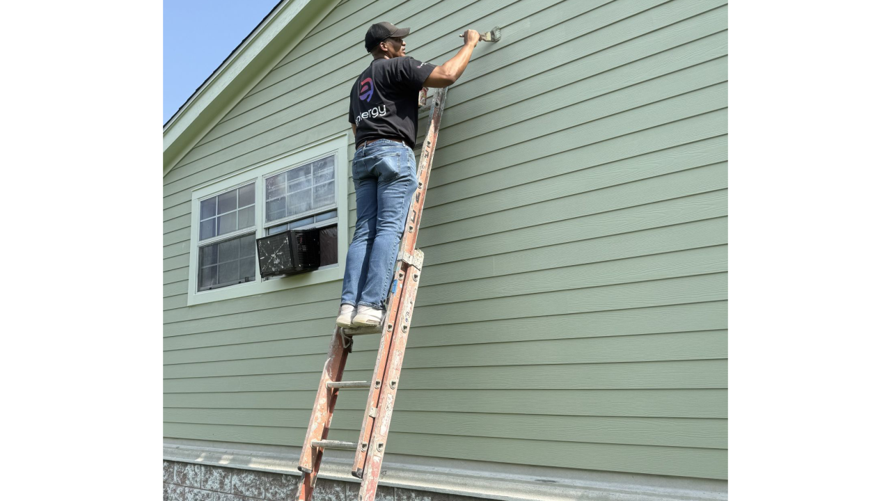 Volunteer on a ladder painting a house exterior