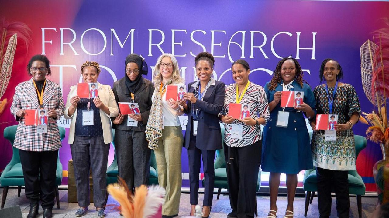 Eight people on a stage, each holding up the same photo