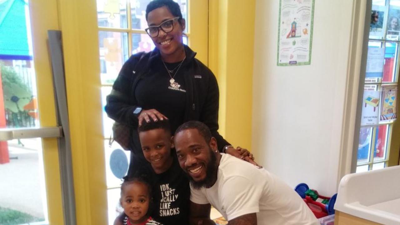 A smiling family posed in a classroom.