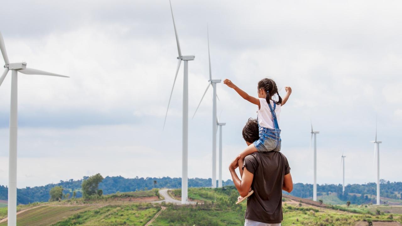 child on adults shoulders looking at wind turbines