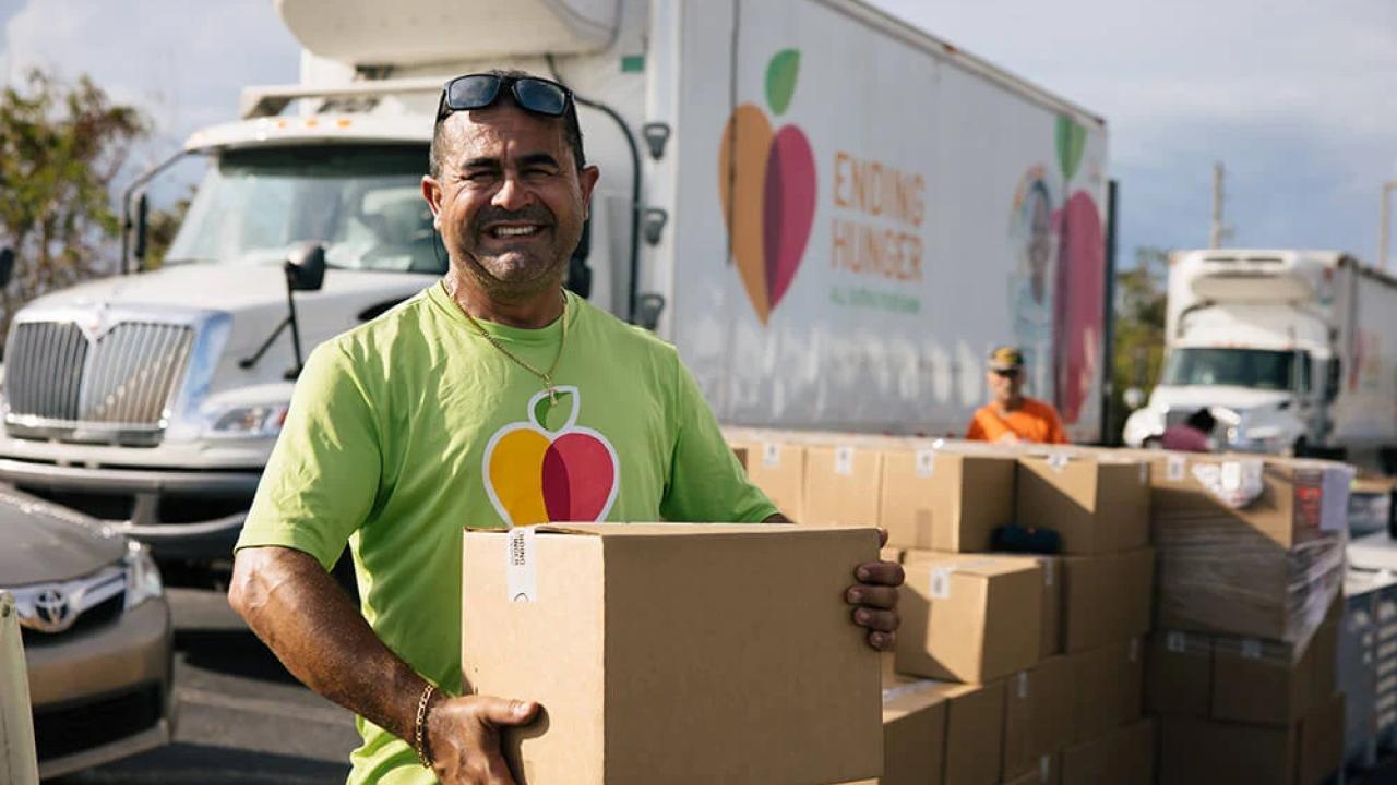 A person holding a box, a stack of boxes and truck behind them