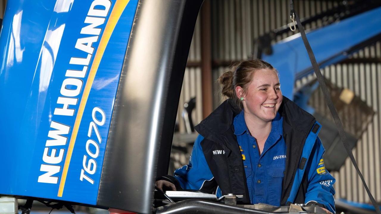 A smiling person looking under the hood of a farming tractor.