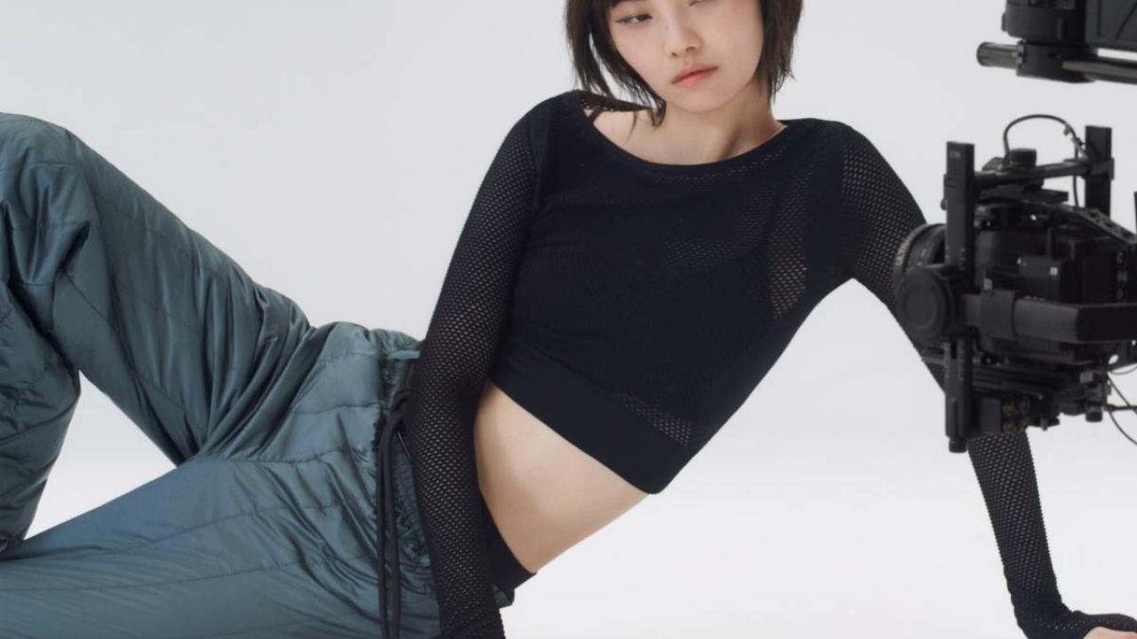 A model sitting on their side on the floor, a camera to the right