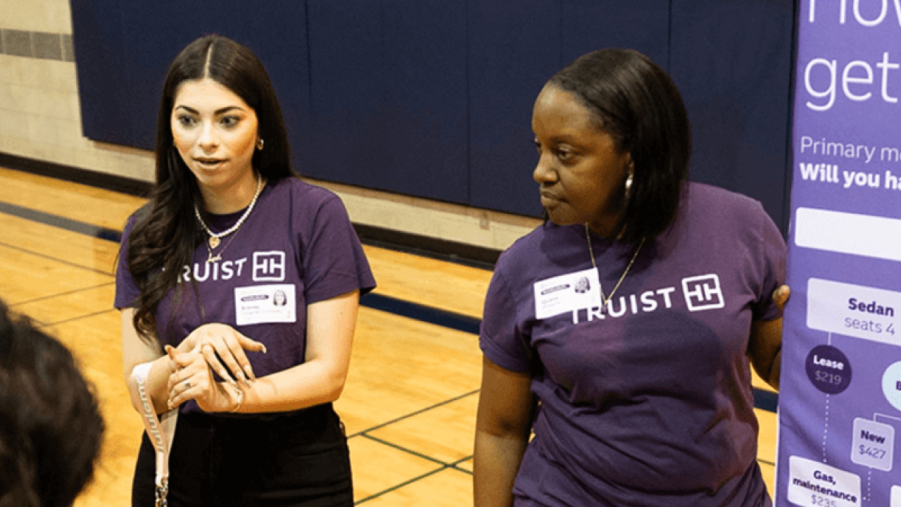 Two Truist employees talking to students in a gymnasium. A display board to the side.