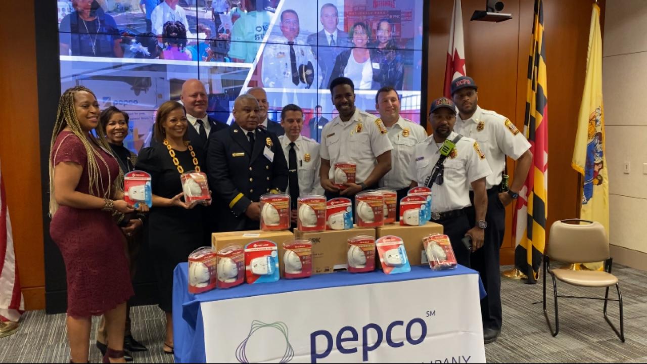 A group of people, some in fire/EMS uniform, behind a table of smoke detectors and a pepco banner.