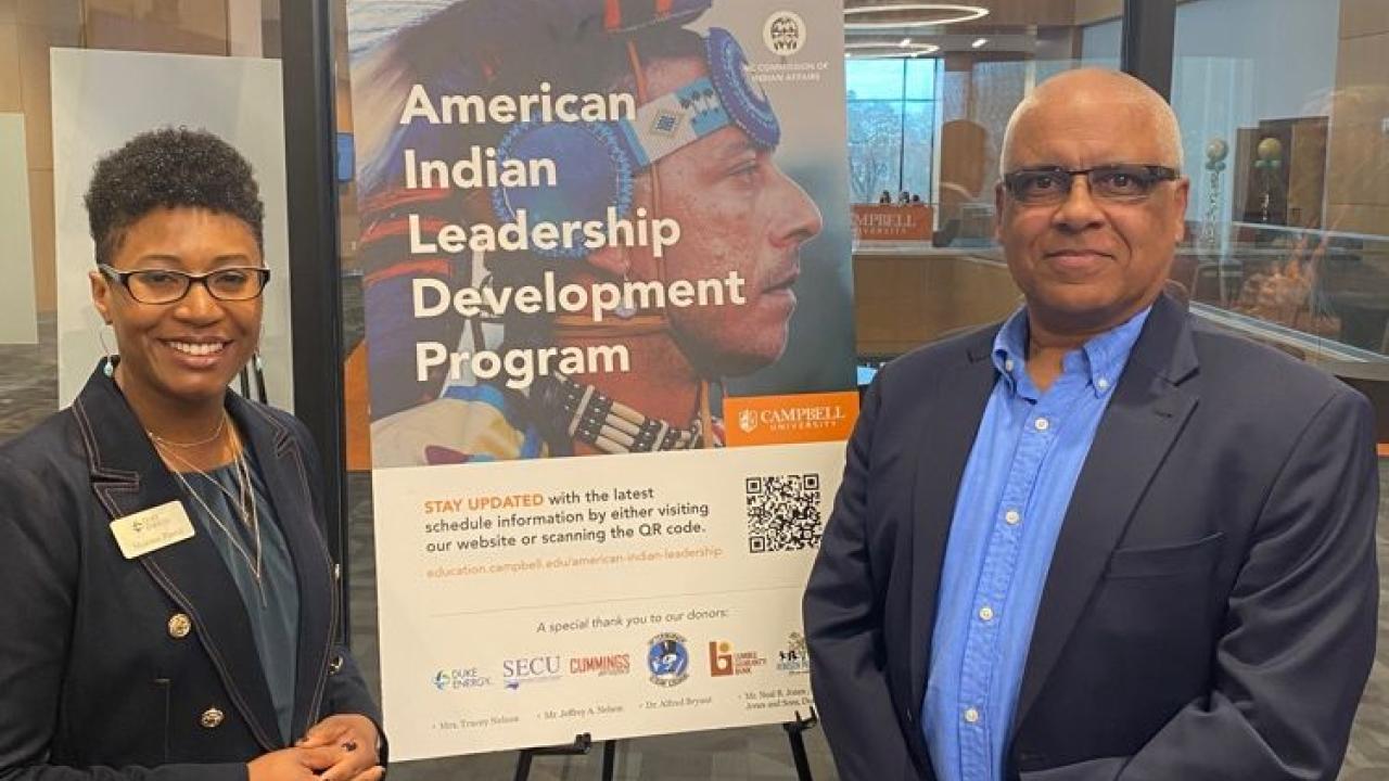 Two people stand beside a poster "American Indian Leadership Development Program."