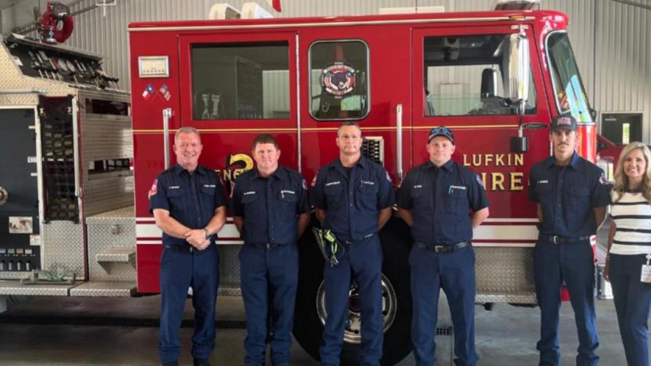 A row of people, some in uniform, in front of a fire truck.