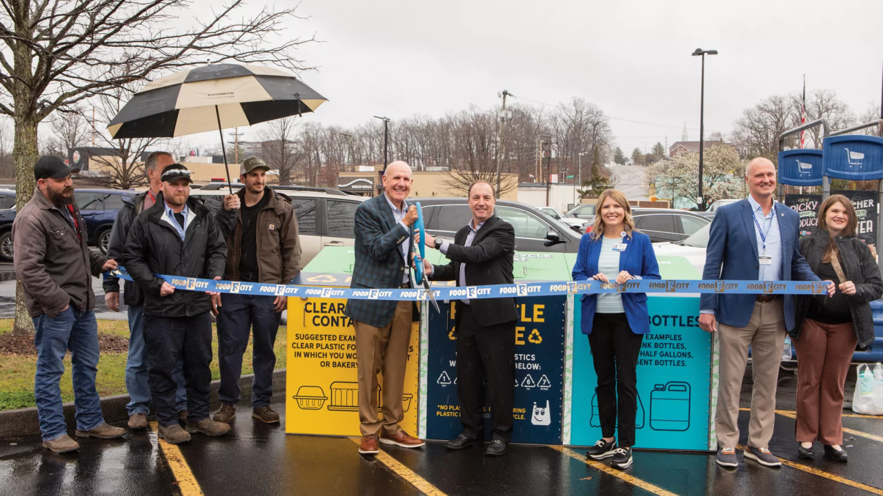 People standing in a parking lot in the rain during a ribbon cutting ceremony