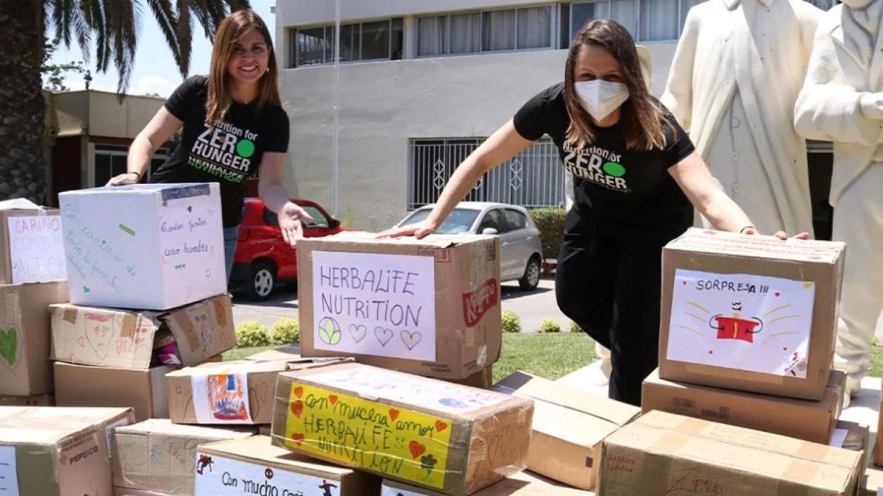 Two volunteers stand outside behind many stacked and hand decorated boxes