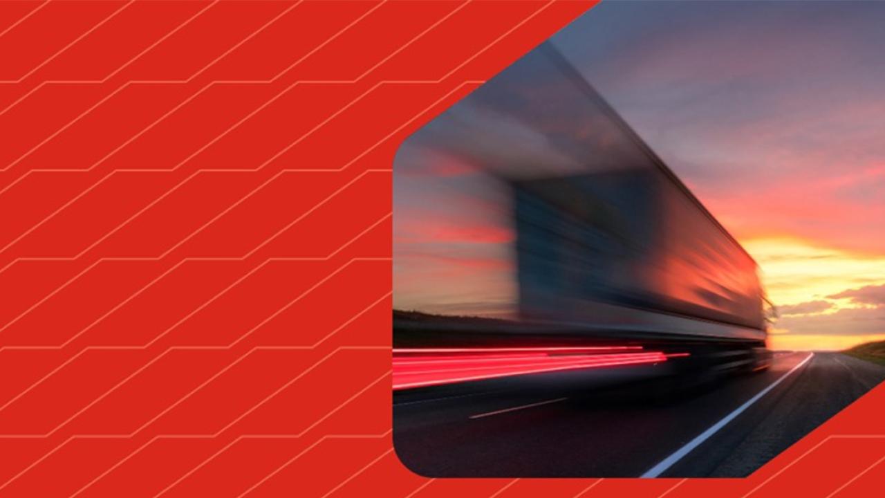 A blurred semitruck driving down a road. On the left a patterned red background