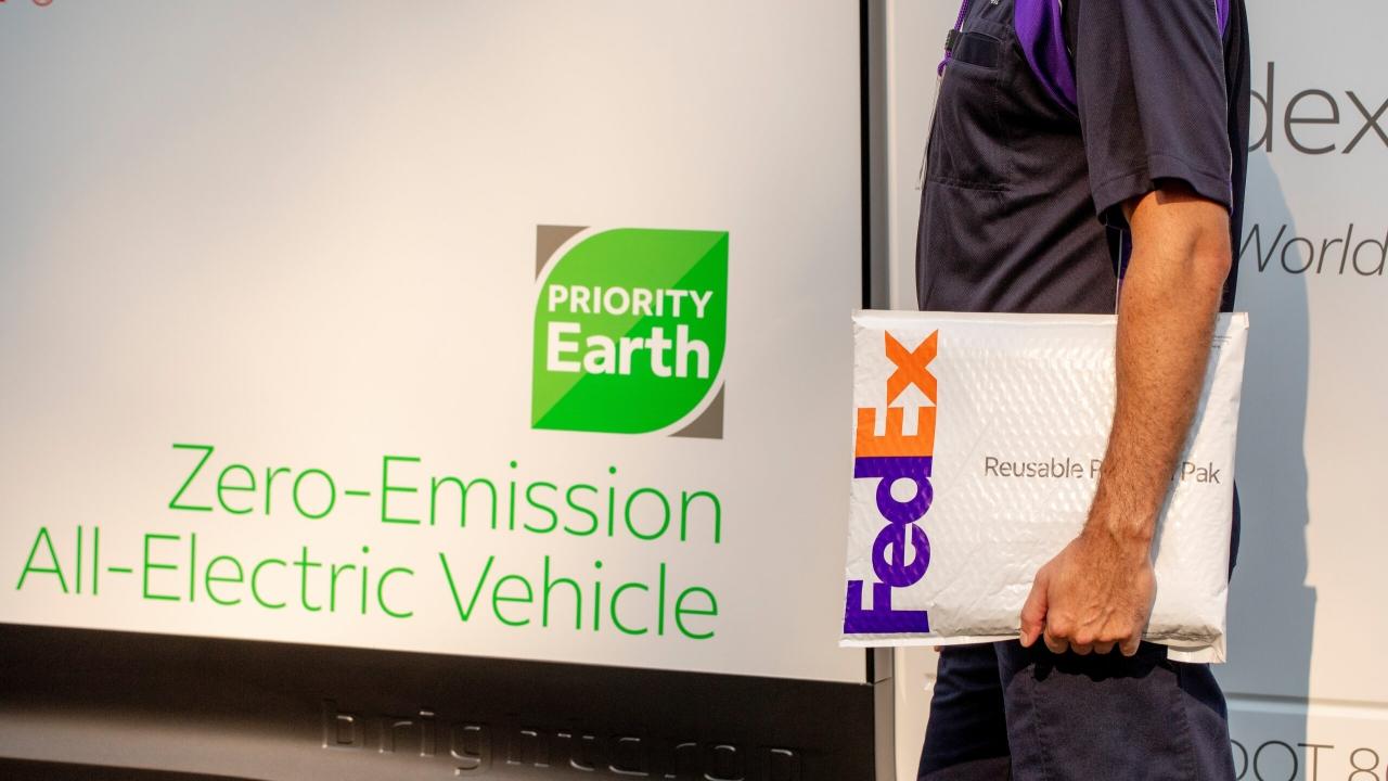 FedEx worker carrying a package in front of a zero-emission all-electric vehicle