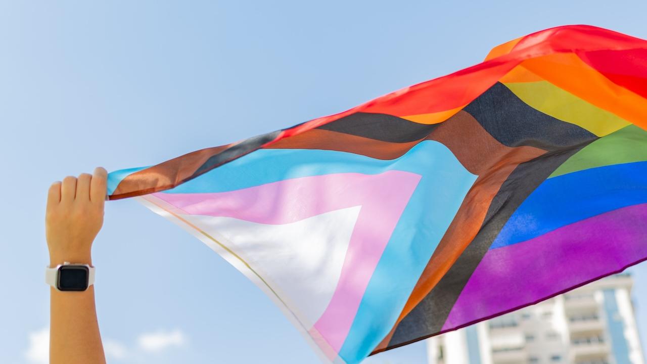 Pride Flag being held up and in the wind.