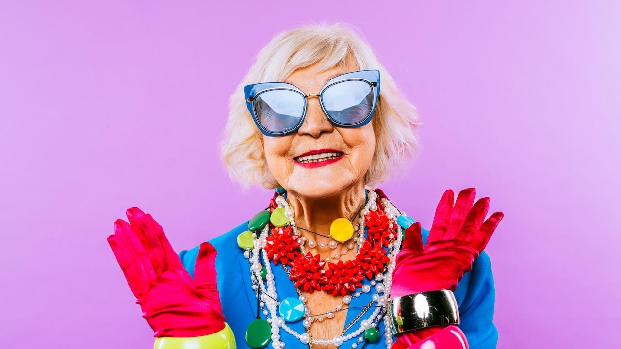 Older, smiling woman wearing big sunglasses and rainbow pride colors for accessories.