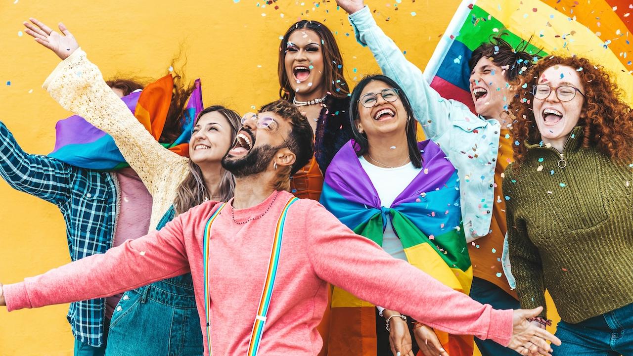 Group of people with a rainbow flag in the background.