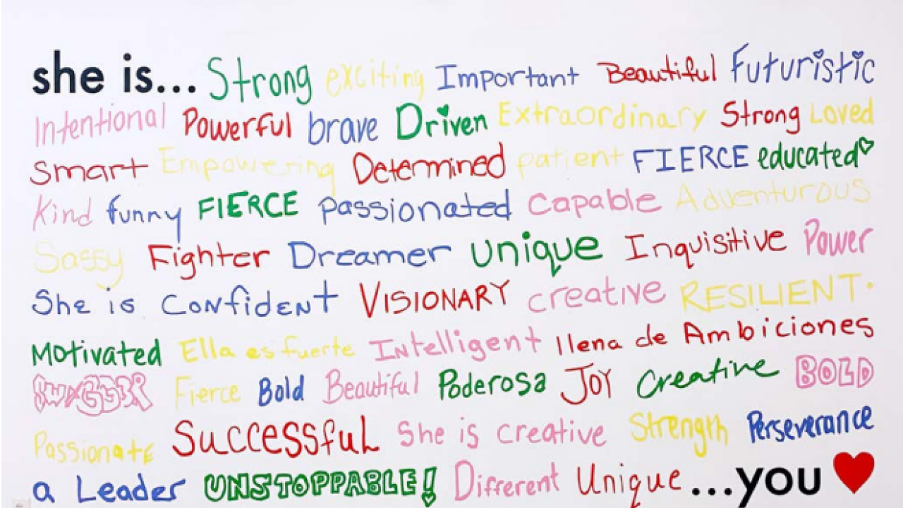 A mural at the Lower East Side Girls Club that says "she is" with many positive adjectives listed in marker below it