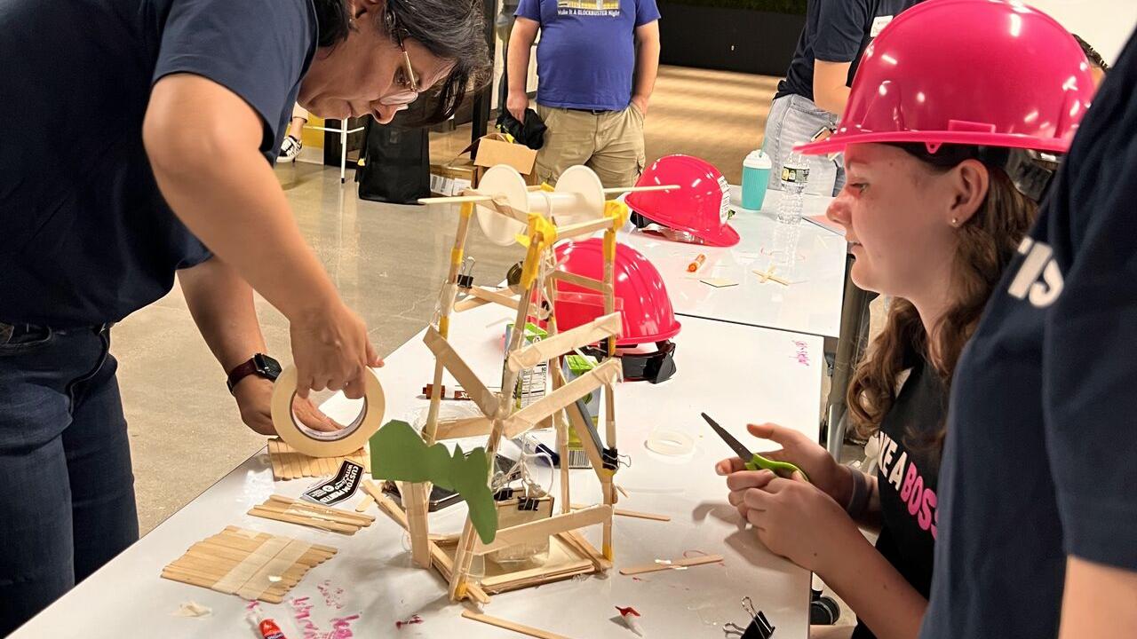 Adult volunteers and children working on building model structures with craft supplies.