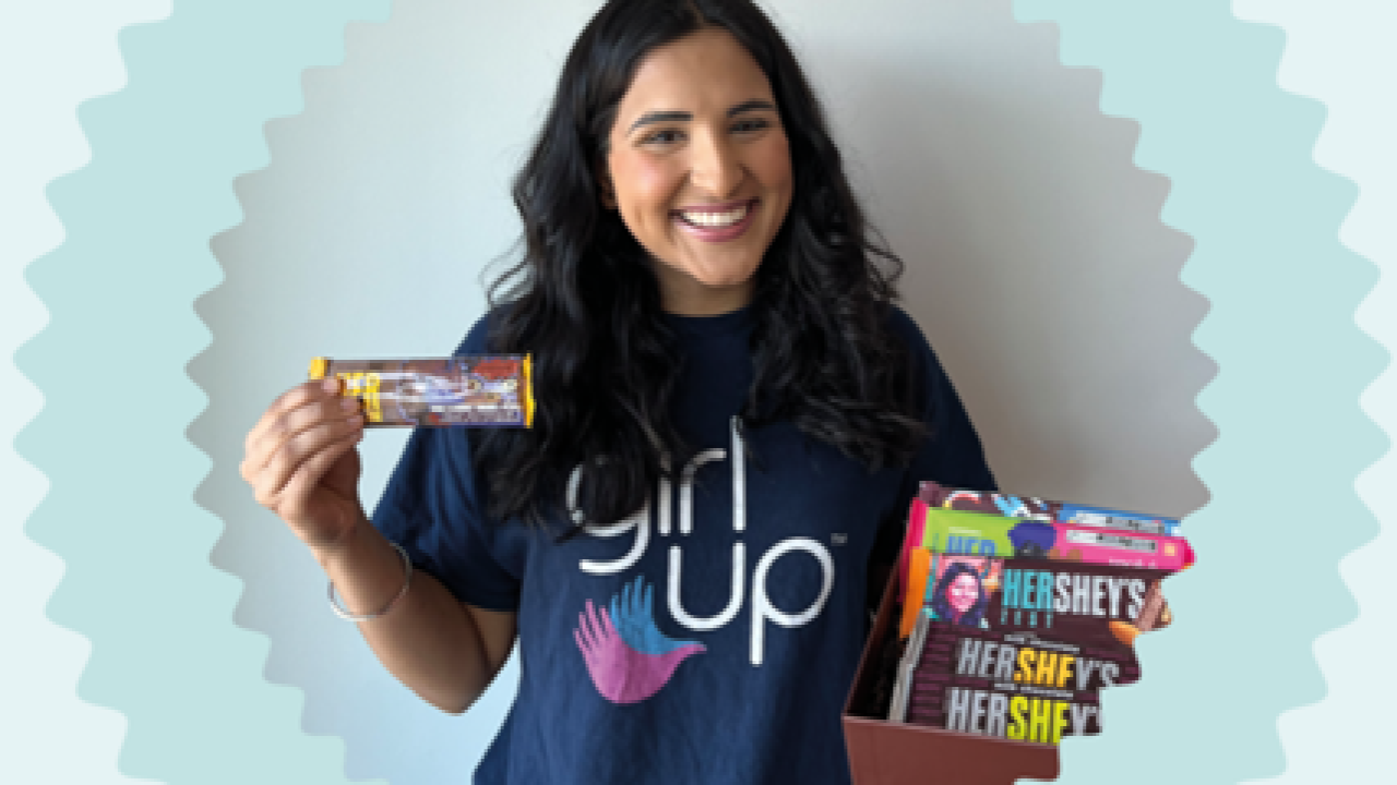 A smiling person wearing a "Girl up" t-shirt, holding up a Hershey bar.
