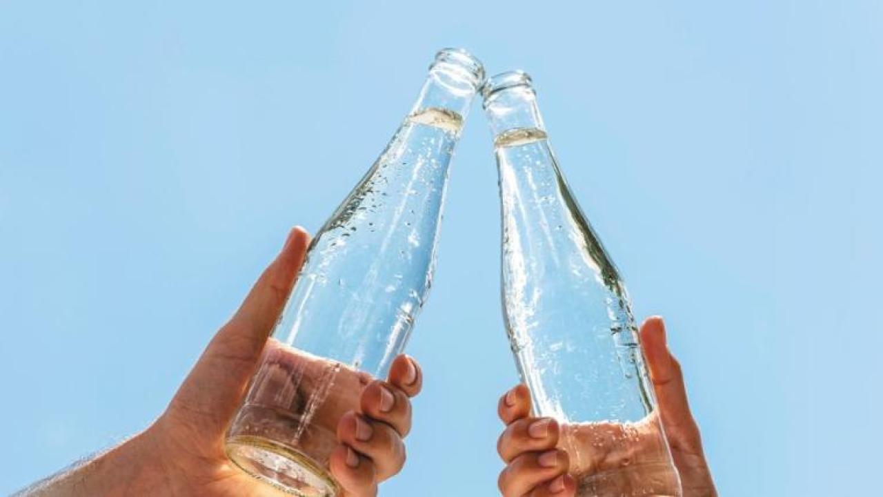 Two hands holding glass bottles, touching at the tops.
