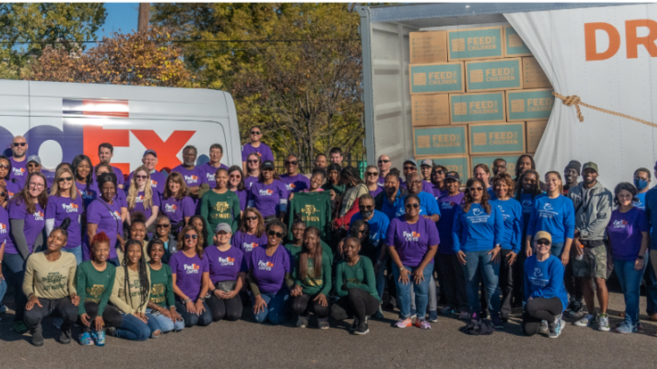 A large group of volunteers posed in front of a FedEx truck and trailer.