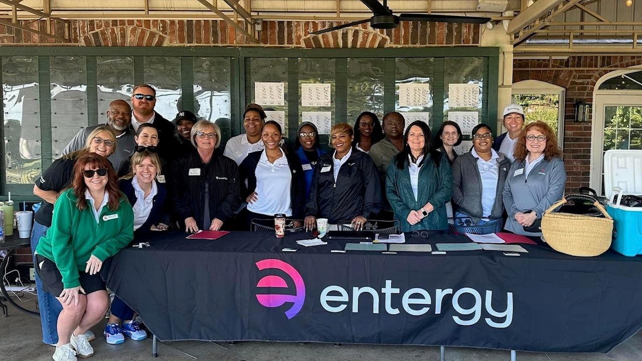 A group posed behind a table with "entergy" logo on the front.