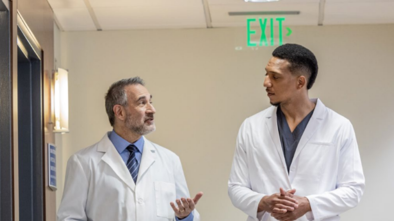 Two medical professionals talking and walking down a hallway.