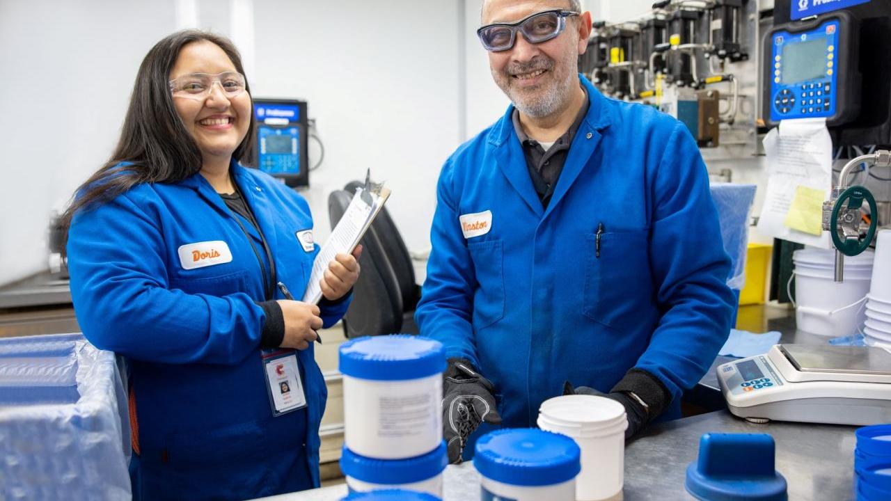 Two people in blue coats smiling in a lab